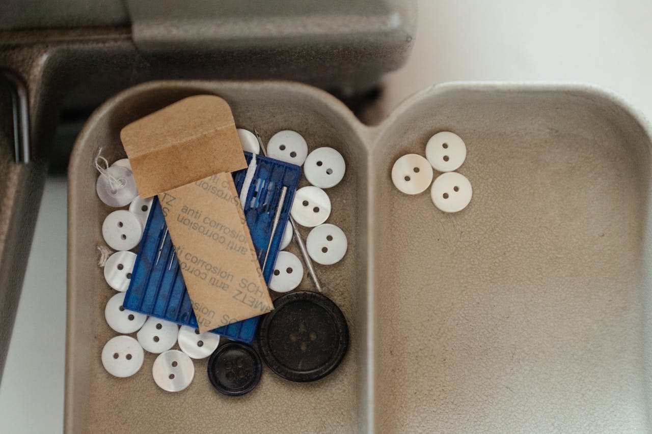 Close-up of a sewing tray with various buttons and needles, ideal for crafting themes.