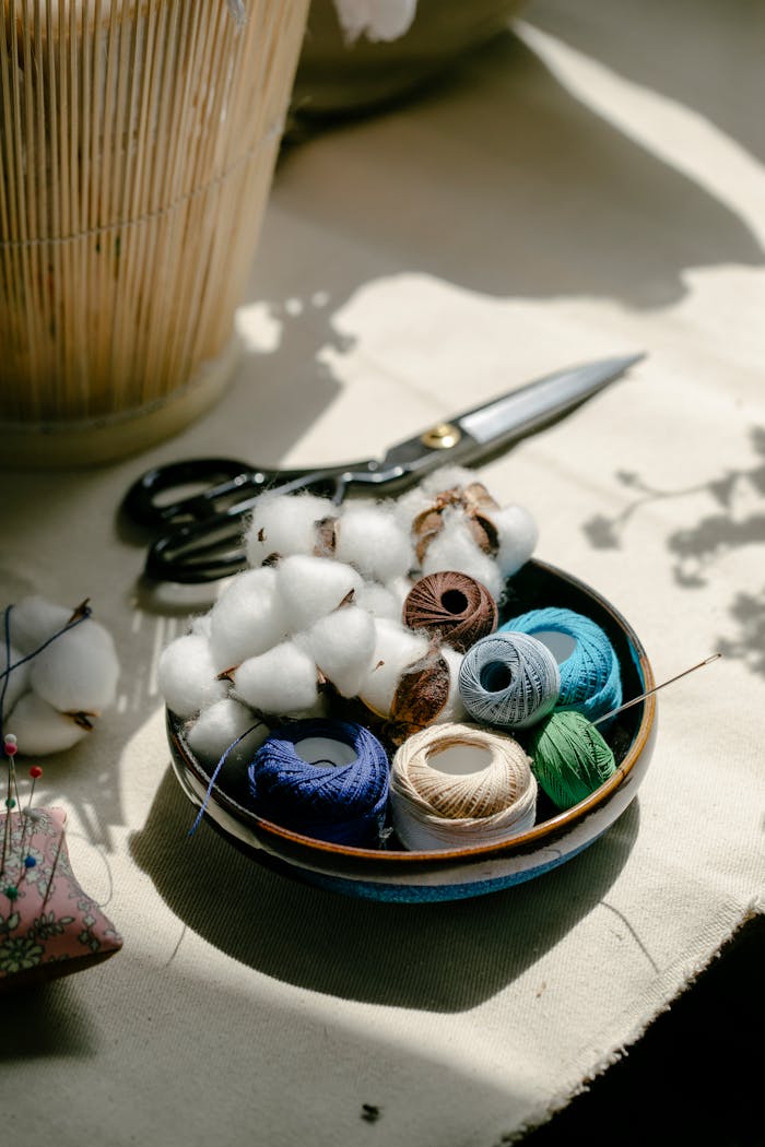 A bowl of colorful threads and cotton under daylight in a workshop setting.